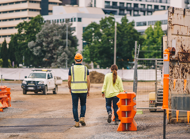 Two construction workers on site walking away from camera