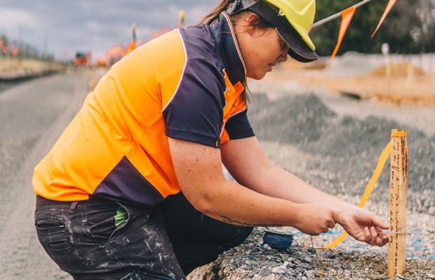 Construction worker in hard hat and high vis marks up worksite with stakes and flags