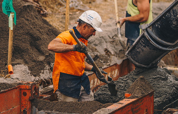 Construction workers in hard hats and his vis shovel concrete