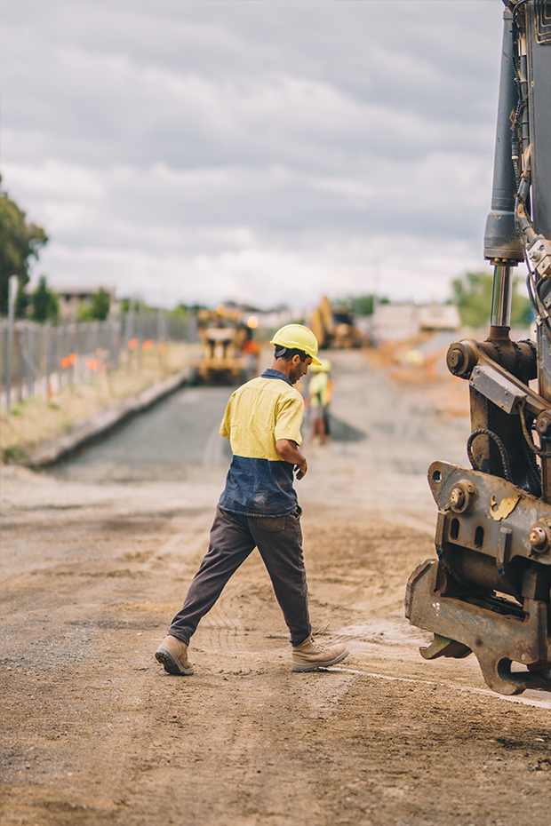 Construction worker working on road walking towards big construction machinery